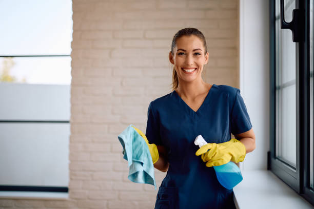 Professional cleaner using cloth and spray bottle while cleaning the house and looking at camera. Copy space.