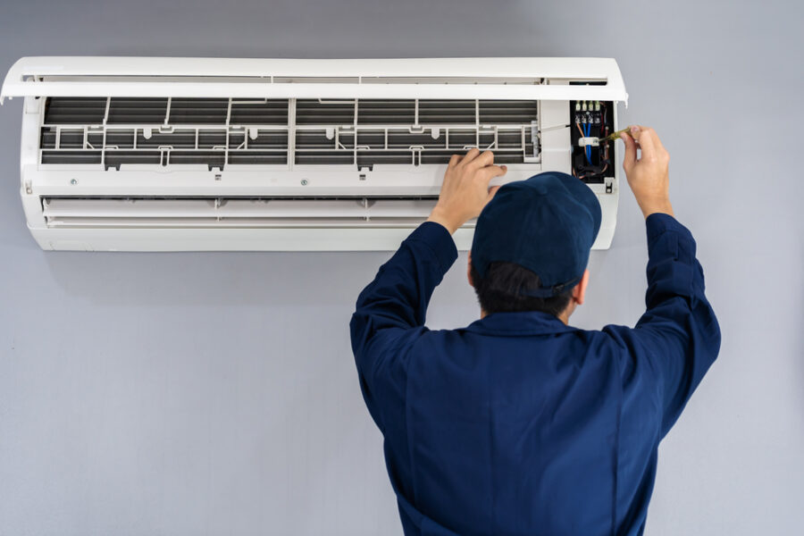 Electrician with screwdriver repairing the air conditioner indoors